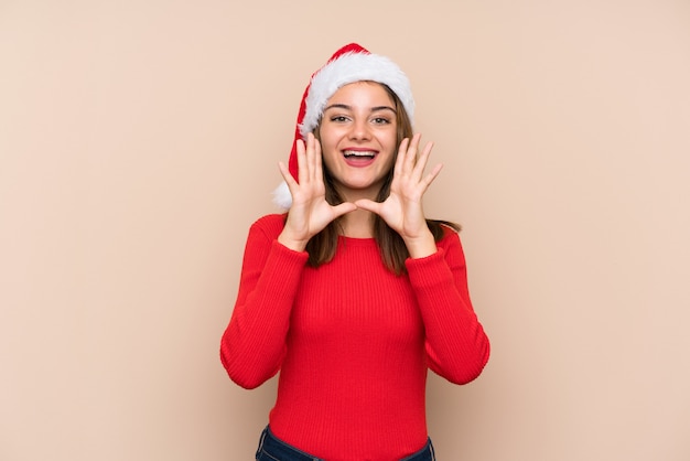 Young girl with christmas hat over isolated wall shouting with mouth wide open