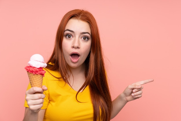 Young girl with a cornet ice cream over isolated wall surprised and pointing side