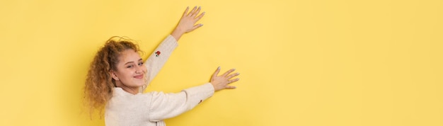 A young girl with curly hair points with a gesture on a studio background