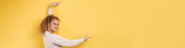 A young girl with curly hair points with a gesture on a studio background