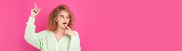 A young girl with curly hair points with a gesture on a studio background