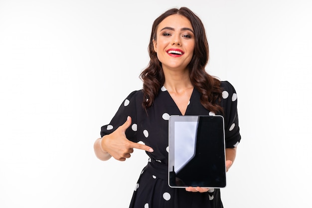 Young girl with delightful smile, in black and white dress in peas recommend a tablet, picture isolated on white background