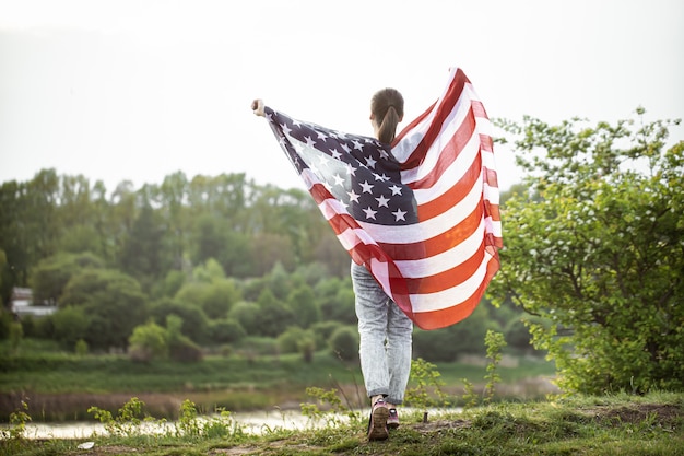 Young girl with the flag of America on nature from the back.