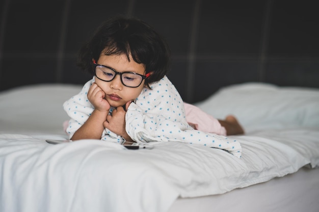 A young girl with glasses is lying on a bed with a laptop.