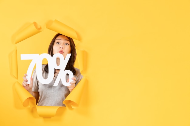 young girl with inscription sign looking through torn yellow paper background money