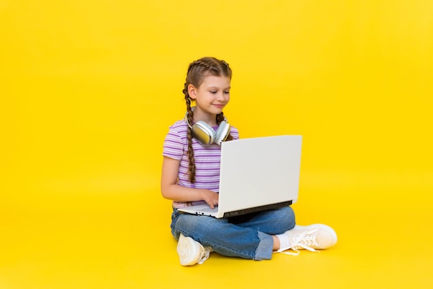 A young girl with a laptop A little girl is sitting on the floor with her legs crossed and holding a laptop Social networking for teenagers Yellow isolated background