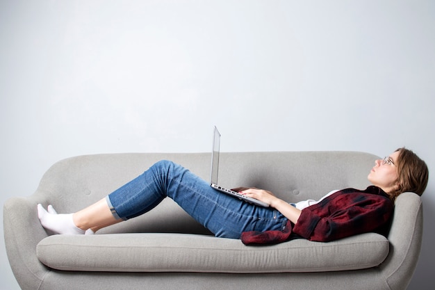 Young girl with a laptop lying on the couch and relax