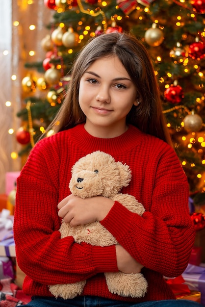 Young girl with long hair in red sweater with teddy bear in her hands Portrait of an attractive girl in Christmas mood