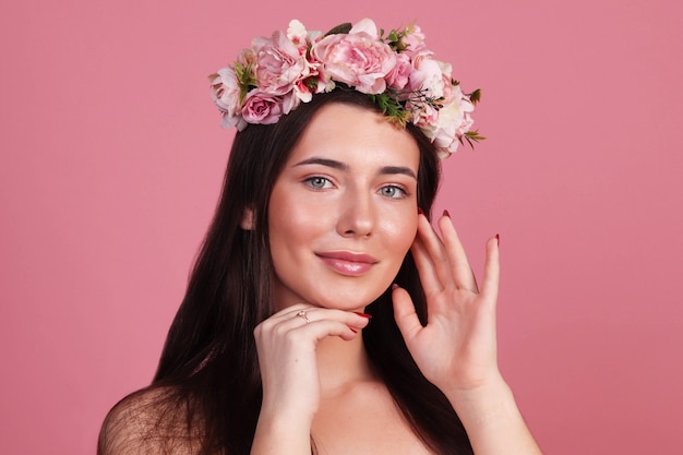 Young girl with natural hair and clean skin in a wreath of flowers on a pink background