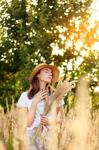 Young girl with outspread hands standing standing in the wheat field at sunset