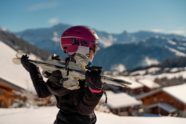 Young girl with a pair of skis and a case of skiing looking at the horizon in a ski resort in the Alps