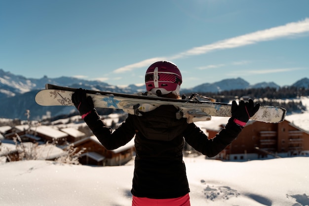 Young girl with a pair of skis and a ski helmet looking at the horizon in a ski resort in the Alps