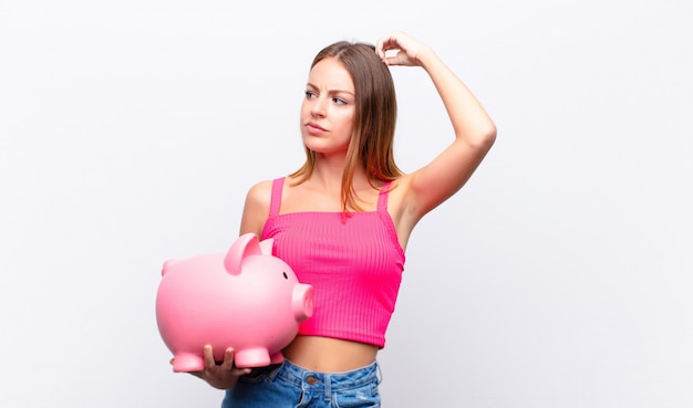 young girl with a piggy bank feeling puzzled and confused doubting