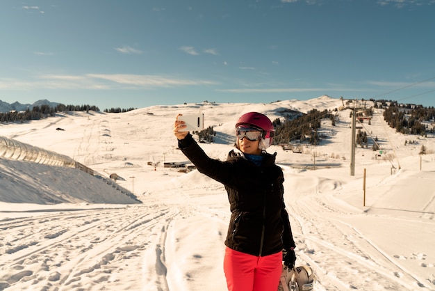 Young girl with ski clothes, a pair of ski goggles and a ski helmet making a selfie in a ski resort