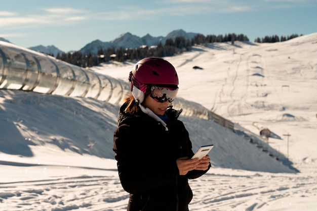 Young girl with a ski helmet consulting her mobile phone in a ski resort in the Alps