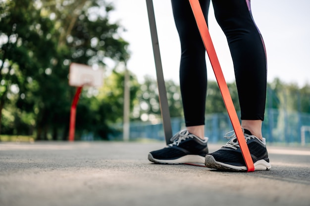 Young girl woman exercising outdoors doing training for her hands and holding rubber elastic bands w...