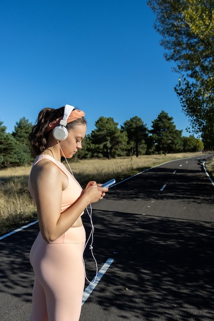 Young girl woman listening to music on an asphalt road on a sunny day Runner girl listening music with headphones on an asphalt road Concept of running woman listening to music on the road