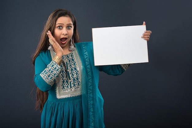 A young girl or woman wearing an Indian traditional dress holding a signboard in her hands on gray background