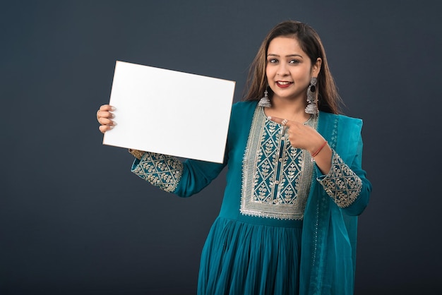 A young girl or woman wearing an Indian traditional dress holding a signboard in her hands on gray background