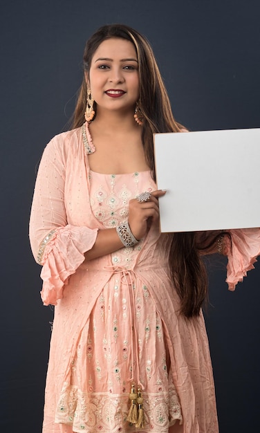 A young girl or woman wearing an Indian traditional dress holding a signboard in her hands on gray background