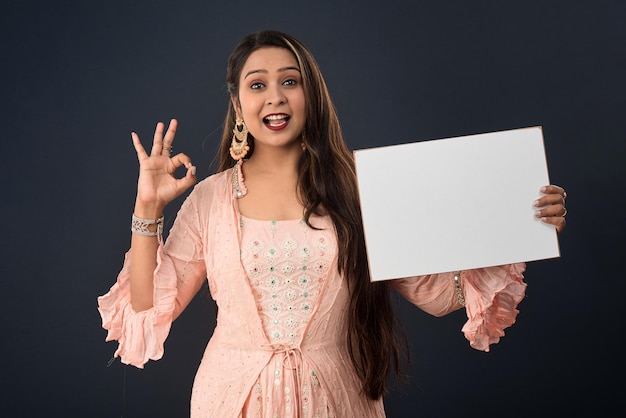 A young girl or woman wearing an Indian traditional dress holding a signboard in her hands on gray background