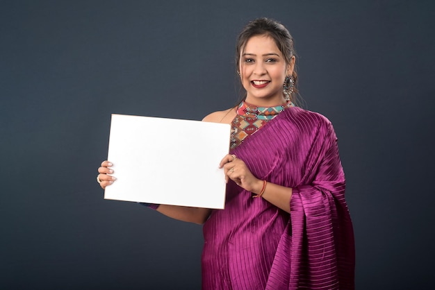 A young girl or woman wearing an Indian traditional saree holding a signboard in her hands on gray background