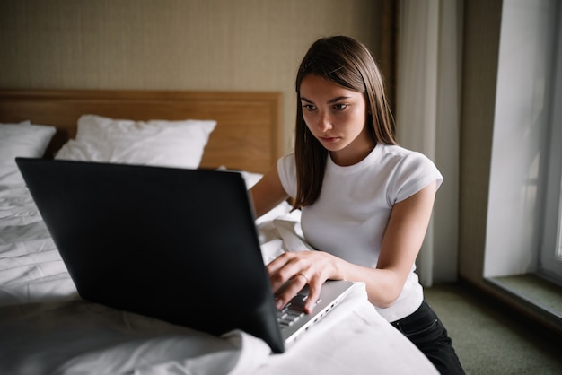 A young girl works on the bed in a laptop