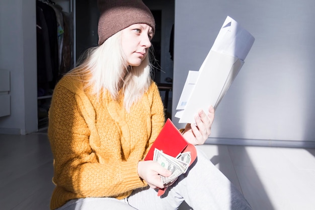 A young girl in a yellow sweater and hat is studying large bills taxes and utility bills