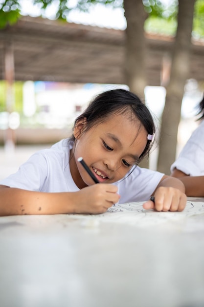 young girls are sitting at a table with markers and coloring books They are drawing and coloring together enjoying their time in the park Concept of fun and creativity