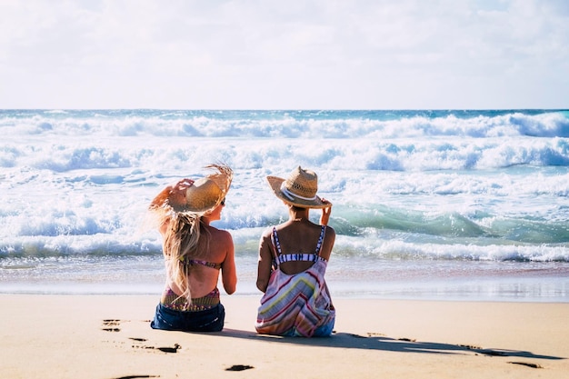 Young girls couple back view enjoy sun and tourism in summer holiday vacation together Relationship and friendship women admiring the ocean blue waves Travel and destination lgbtq concept lifestyle