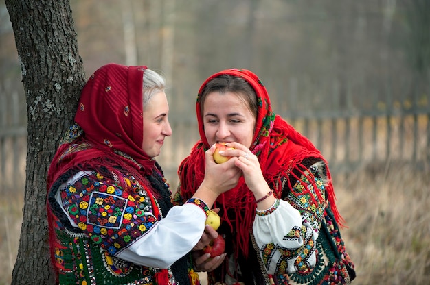 Young girls dressed in ancient picturesque Hutsul national clothes eat an apple. Ukraine.