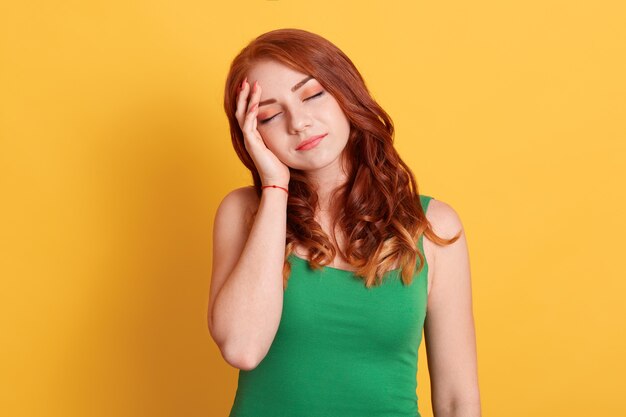 Young good looking red haired female stands with closed eyes isolated