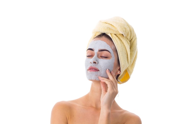 Young goodlooking woman with blue cosmetic mask on her face and yellow towel on her head in studio