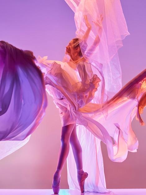 Young graceful female ballet dancer or classic ballerina dancing at pink studio