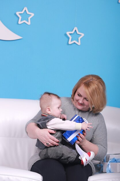 Young grandmother with her little grandson on a white sofa. Blue wall with a white moon and stars on a wall.