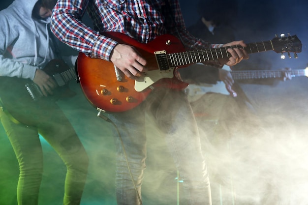 Young group playing electric guitar on lighted foggy background