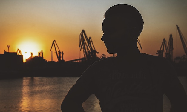 Young guy on the background of the port in the setting sun. summer evening. darkened atmosphere