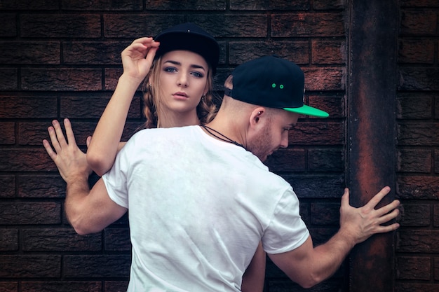 Young guy in black pants and a white t-shirt poses with a beautiful blonde girl outdoors.