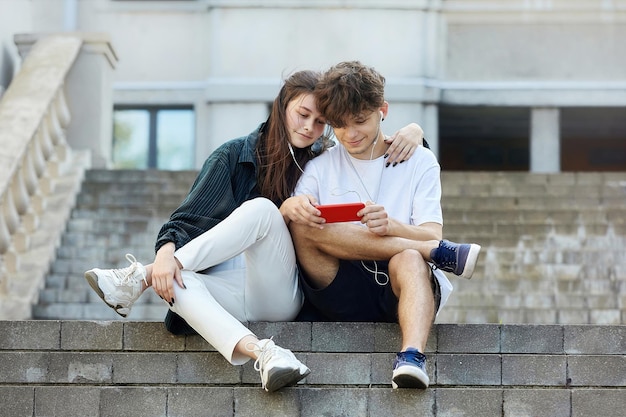 Young guy and a girl sitting on the street look into a red smartphone with a smile