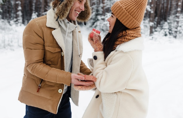 A young guy gives a gift to a girl in a snow-covered forest. Surprise for Valentine's Day.