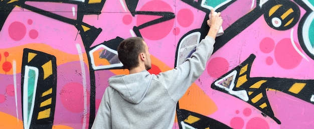 A young guy in a gray hoodie paints graffiti in pink and green c