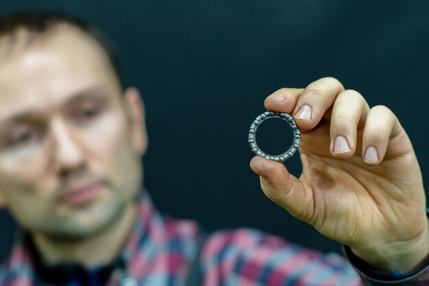 A young guy holds a bearing in his hand on a black background A bicycle mechanic in the workshop changes bearings for the steering column Repair of motorcycles and cars in the service center