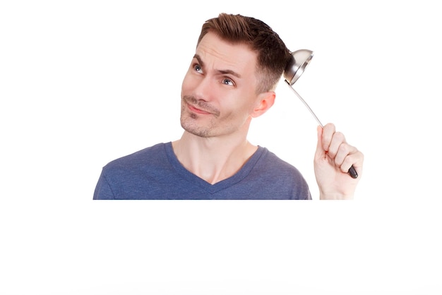 A young guy is holding a kitchen ladle on a white background. Male housekeeper or houseworker. Kitchenware and cuisine concept. Copy space.