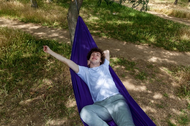 A young guy is resting in a purple hammock in nature enjoying loneliness and silence