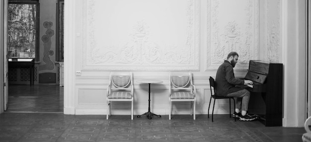 A young guy plays the piano in a large white hall black and white