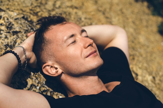 Young guy rests closing his eyes lying on stone Closeup portrait