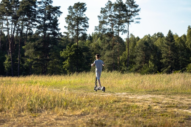 A young guy rides an electric scooter on a dirt road in the forest