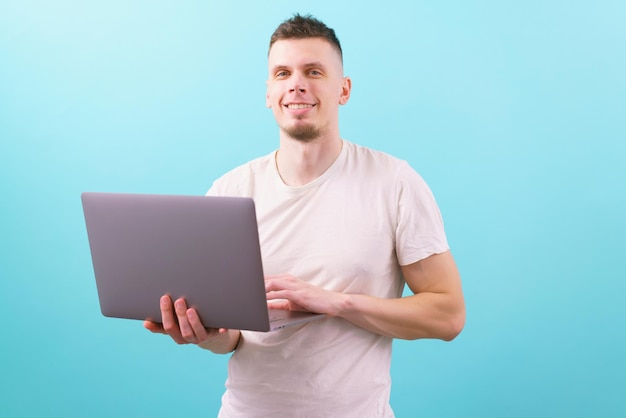 The young guy smiling holding a laptop and looking at the camera on a blue Man Laptop Using Male