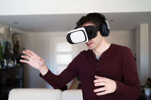 Young guy wearing VR glasses at home and moving arms