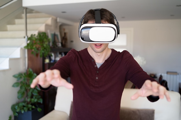 Young guy wearing VR glasses at home and moving arms